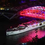 Francouzská loď projíždí pod rozsvíceným mostem v národní trikolóře