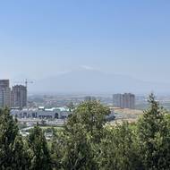 Pohled z kopce Tsitsernakaberd od památníku na horu Ararat, která je zahalena mlhou a je vidět zejména její bílá čepice. 